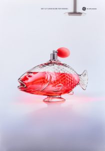 A poster of a perfume bottle in the shape of a fish with red liquid and an exhaust fan in the distance.