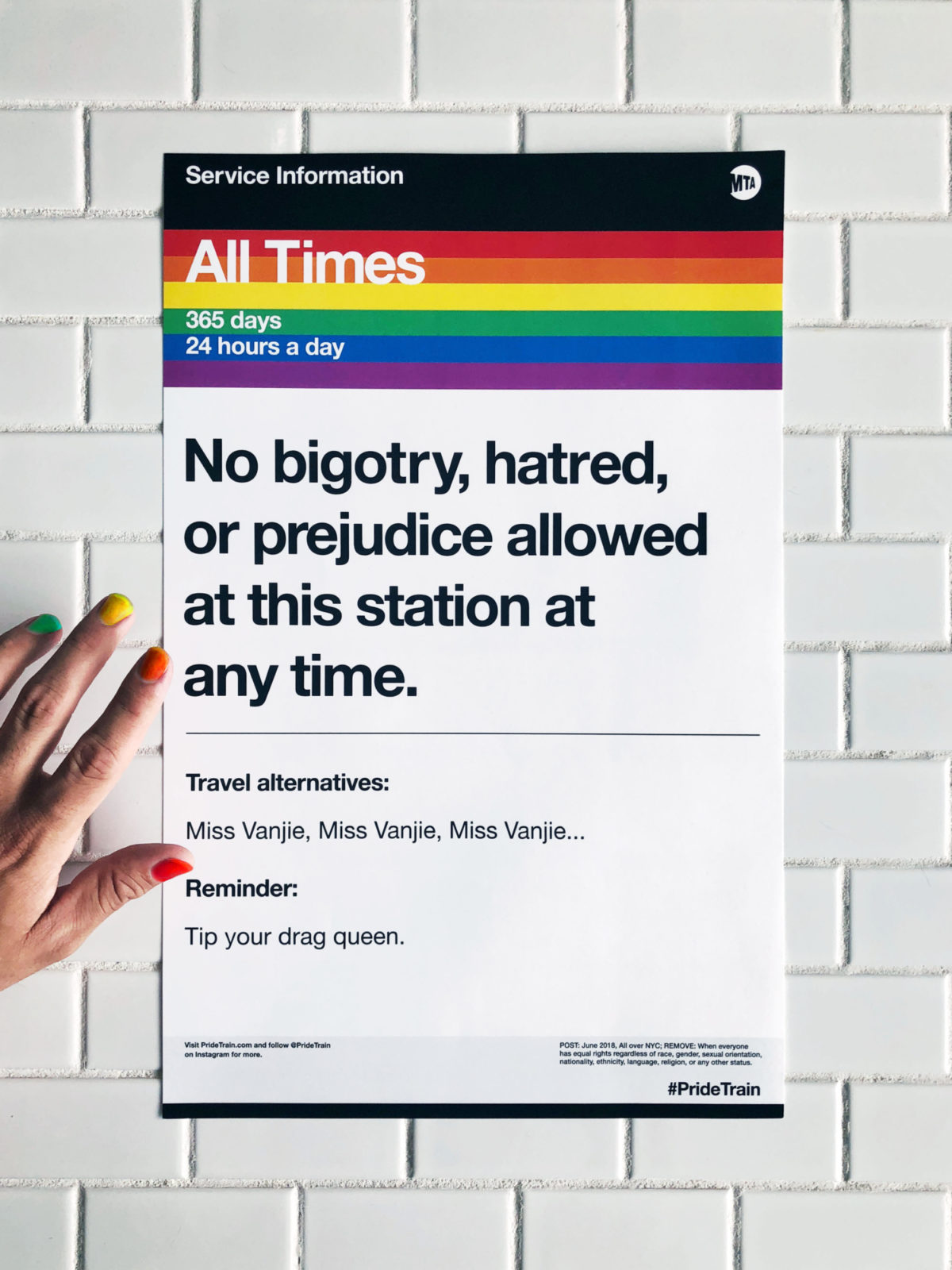 A hand is holding a flyer, with the pride flag, that is announcing a train message.