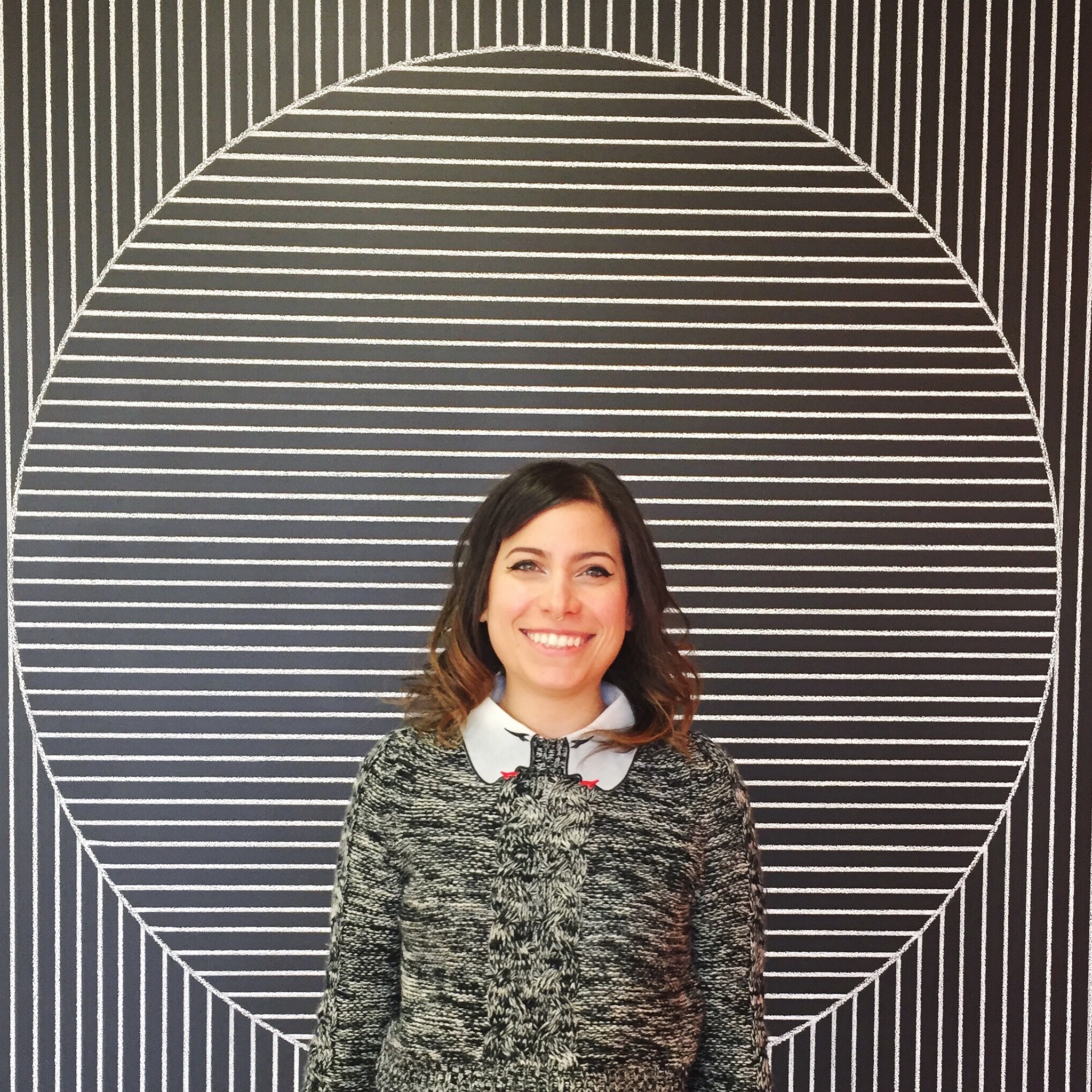 A woman smiling against a black and white striped background.