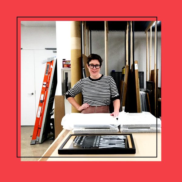 The Collections Manager smiling in front of stacked covered art frames in the archives room.