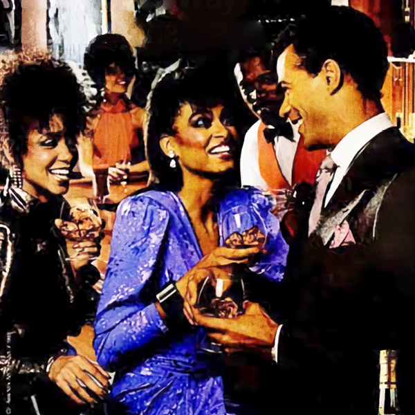 A cropped image featuring two Black women and a Black man laughing and drinking in a bar.