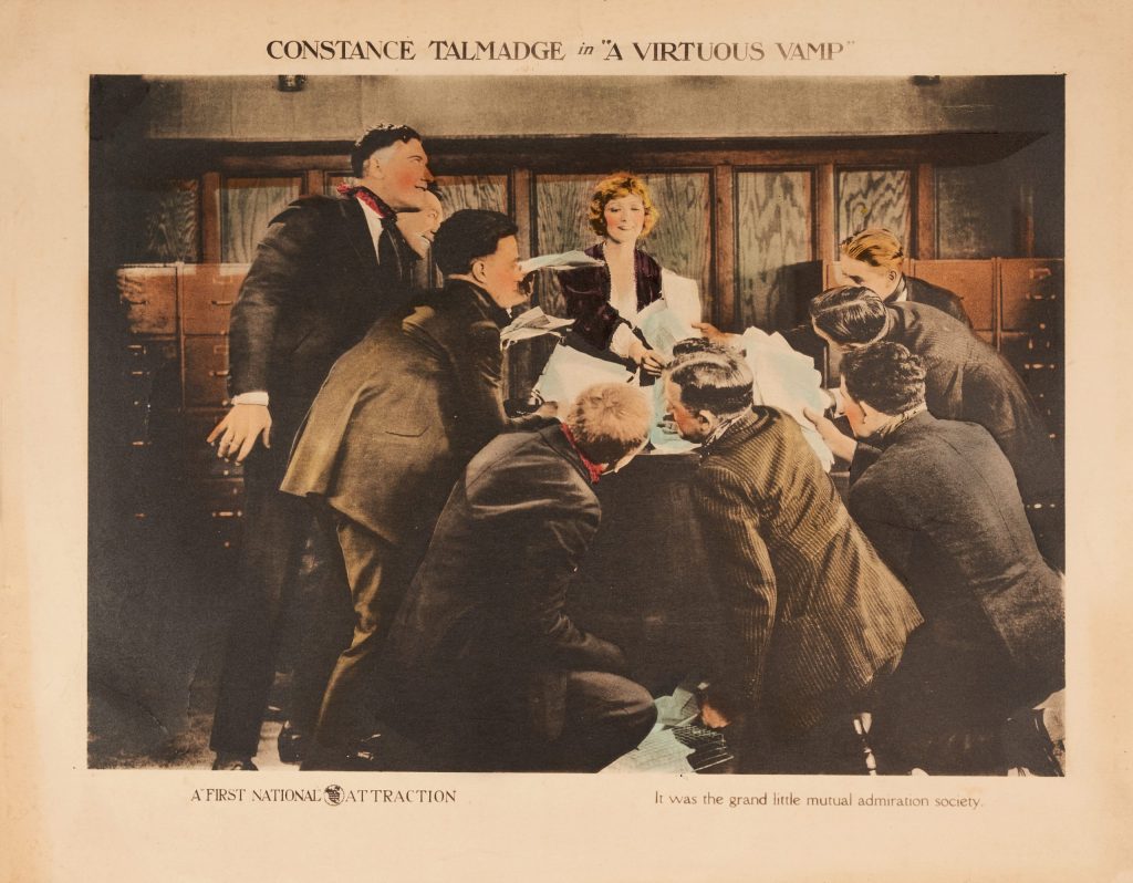 A photographic lobby card of a woman surrounded by a group of men.