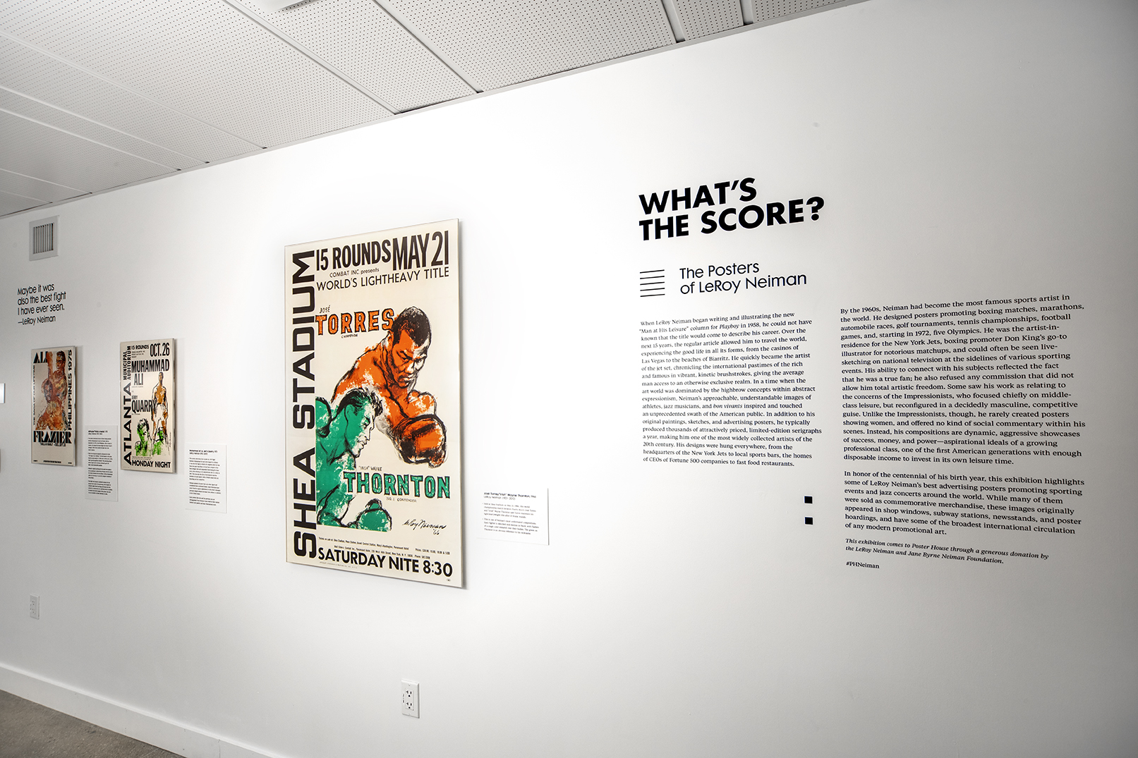 A white exhibition wall of posters with American boxers painted in hues of green and orange.