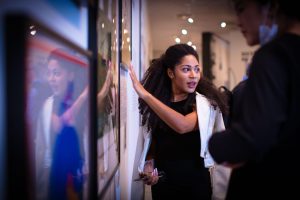 A Black woman in a black dress pointing to an image on display at an art museum.