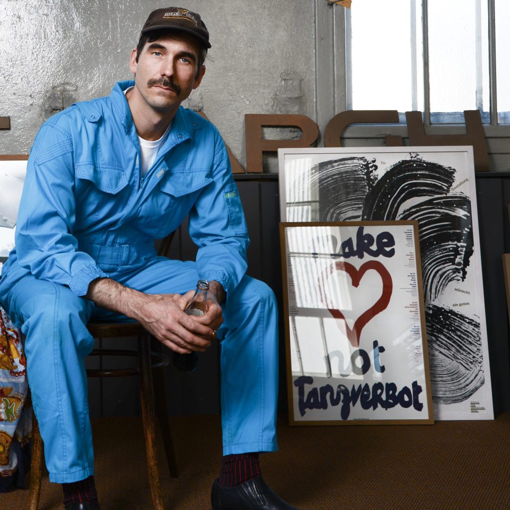 A photo image of a man in blue coveralls sitting next to two printed images in frames.