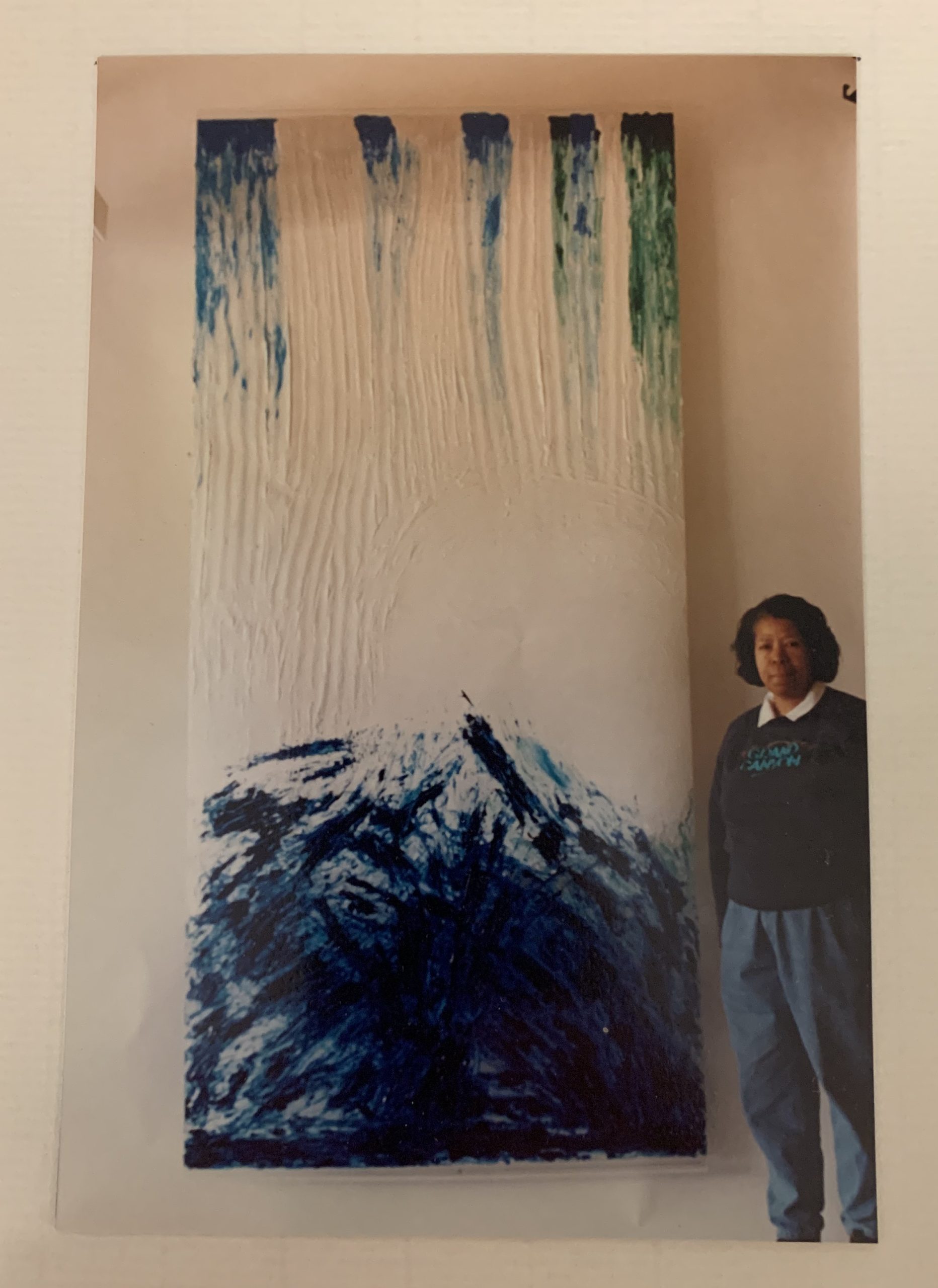 A Black woman stands by an art piece featuring the image of a mountain.