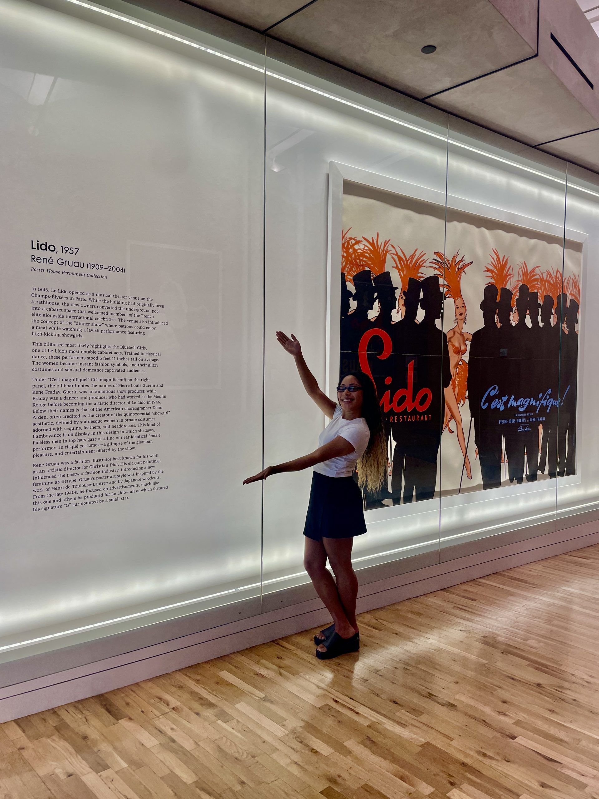 Photograph of a young woman gesturing enthusiastically to wall text.