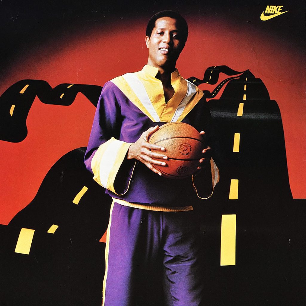 A Black man in a purple jumpsuit holds a basketball in hand