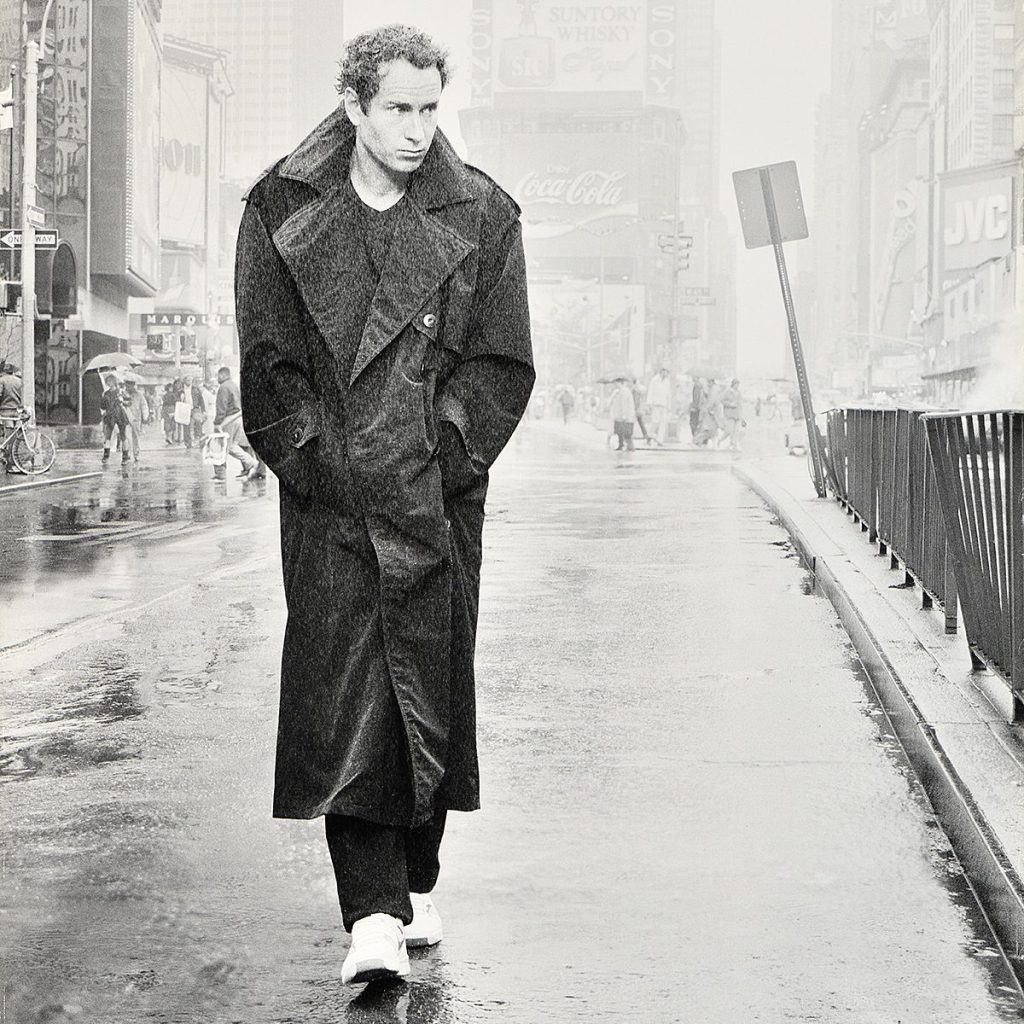 A man in a dark coat walks a street