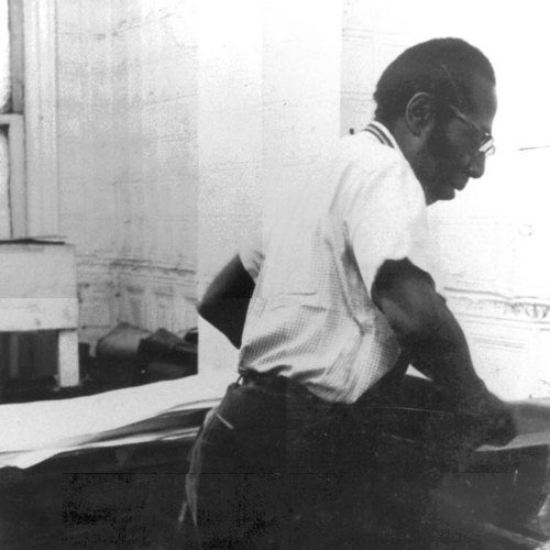 A black and white photograph of Robert Blackburn working on a stone lithograph.