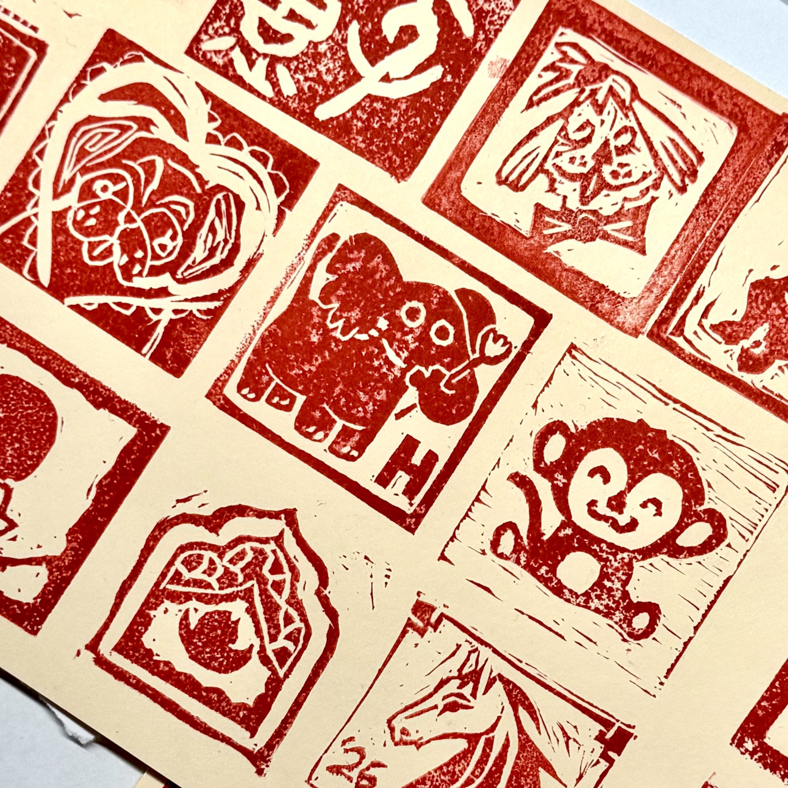 an off-white piece of paper with block printed images printed in red ink and arranged in a grid, depicting a monkey, an elephant, a dog, and other images.