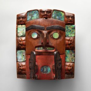 A square, wooden sculpture of a face.