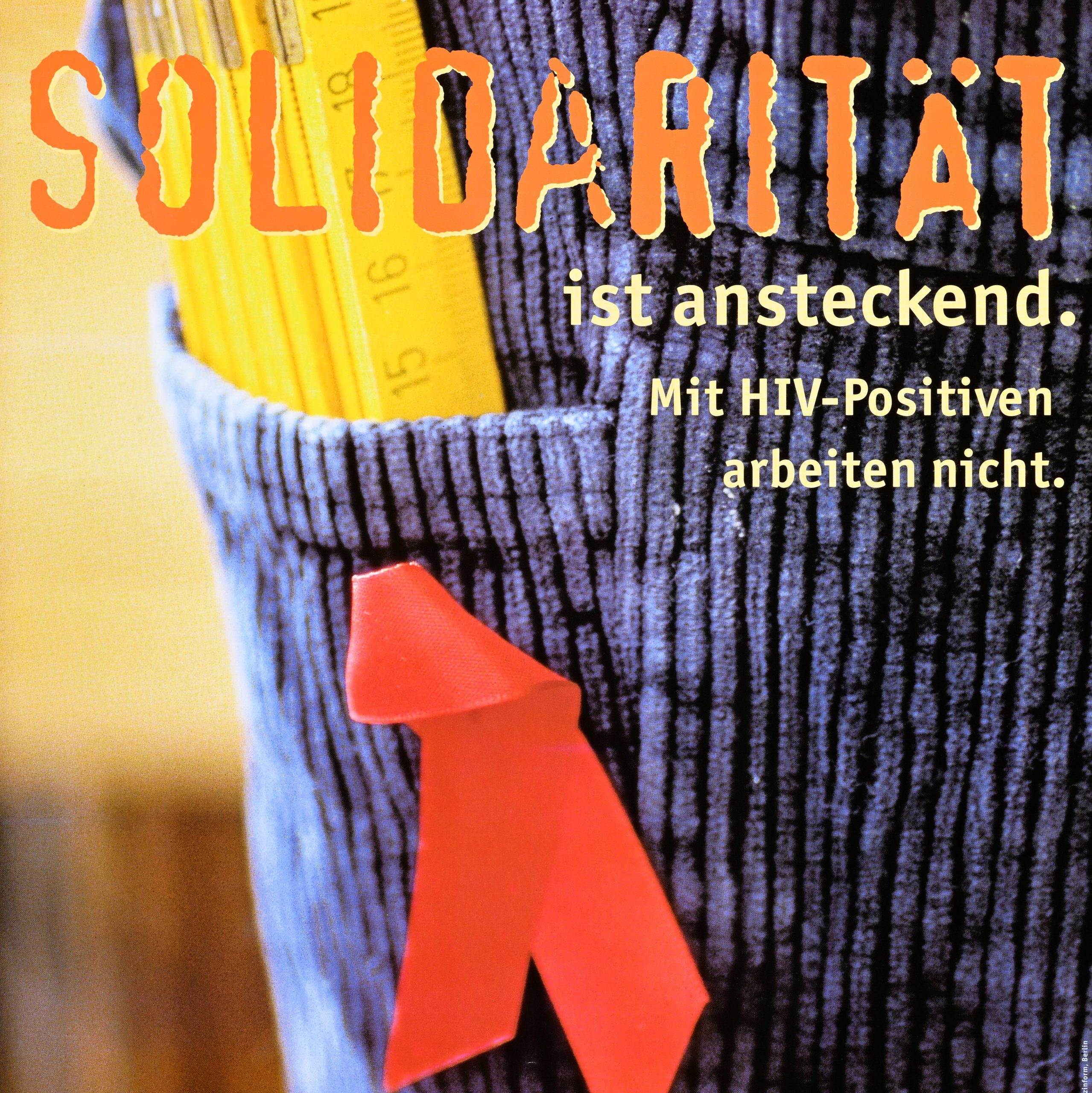 A german poster with a close up image of a red ribbon, the symbol of solidarity with people living with HIV/AIDS, pinned to a blue corduroy garment.