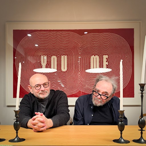 Two men sitting at a table in front of a framed print that says the words 